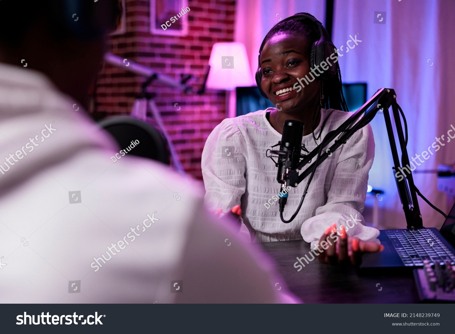 Female vlogger interviewing male guest on podcast show, using recording equipment. Happy woman streaming live broadcast episode with man in studio to record conversation for channel. #2148239749