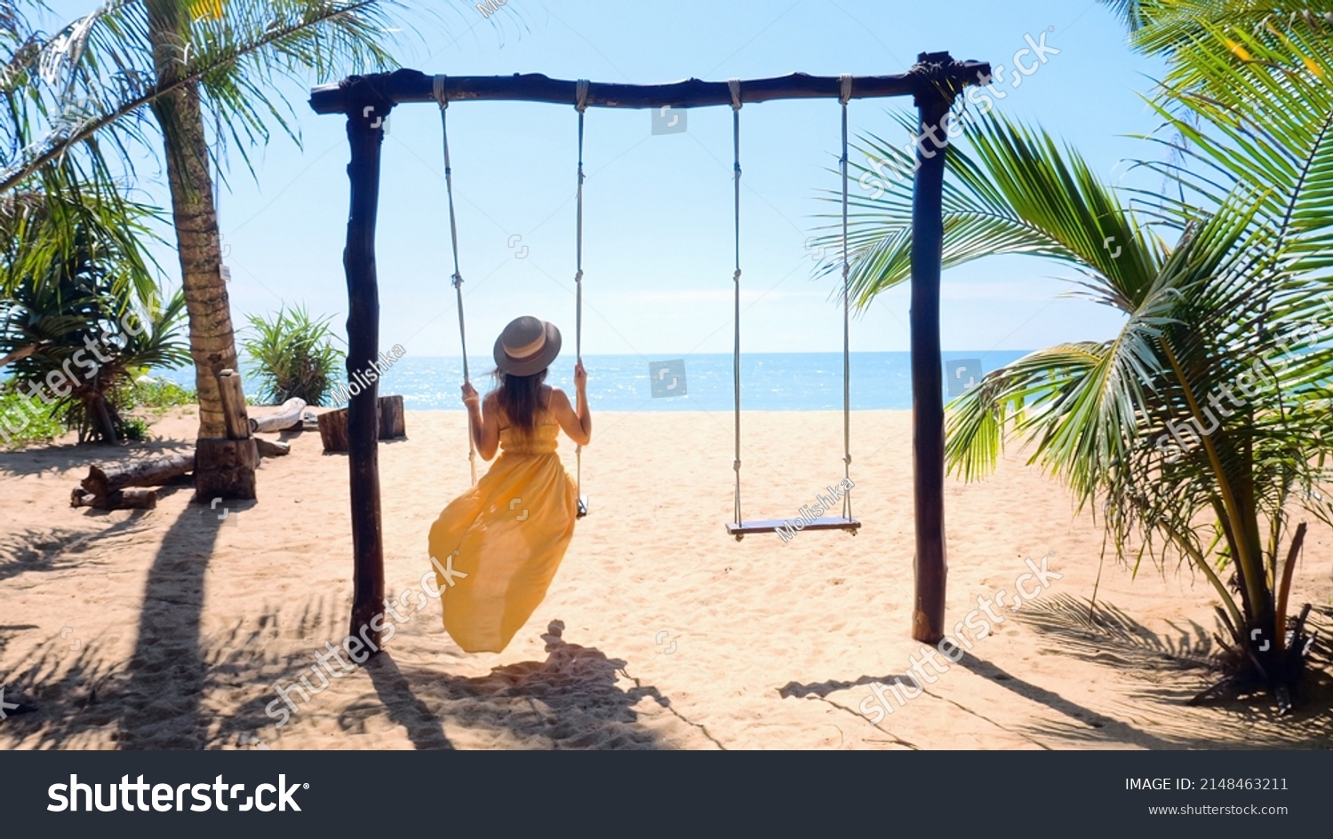Woman tourist swinging on swing, sandy beach with palm trees and blue sea on background. Tropical vacation. Girl in yellow dress on summer holidays, fun on sunny coastal, good mood, romantic. #2148463211