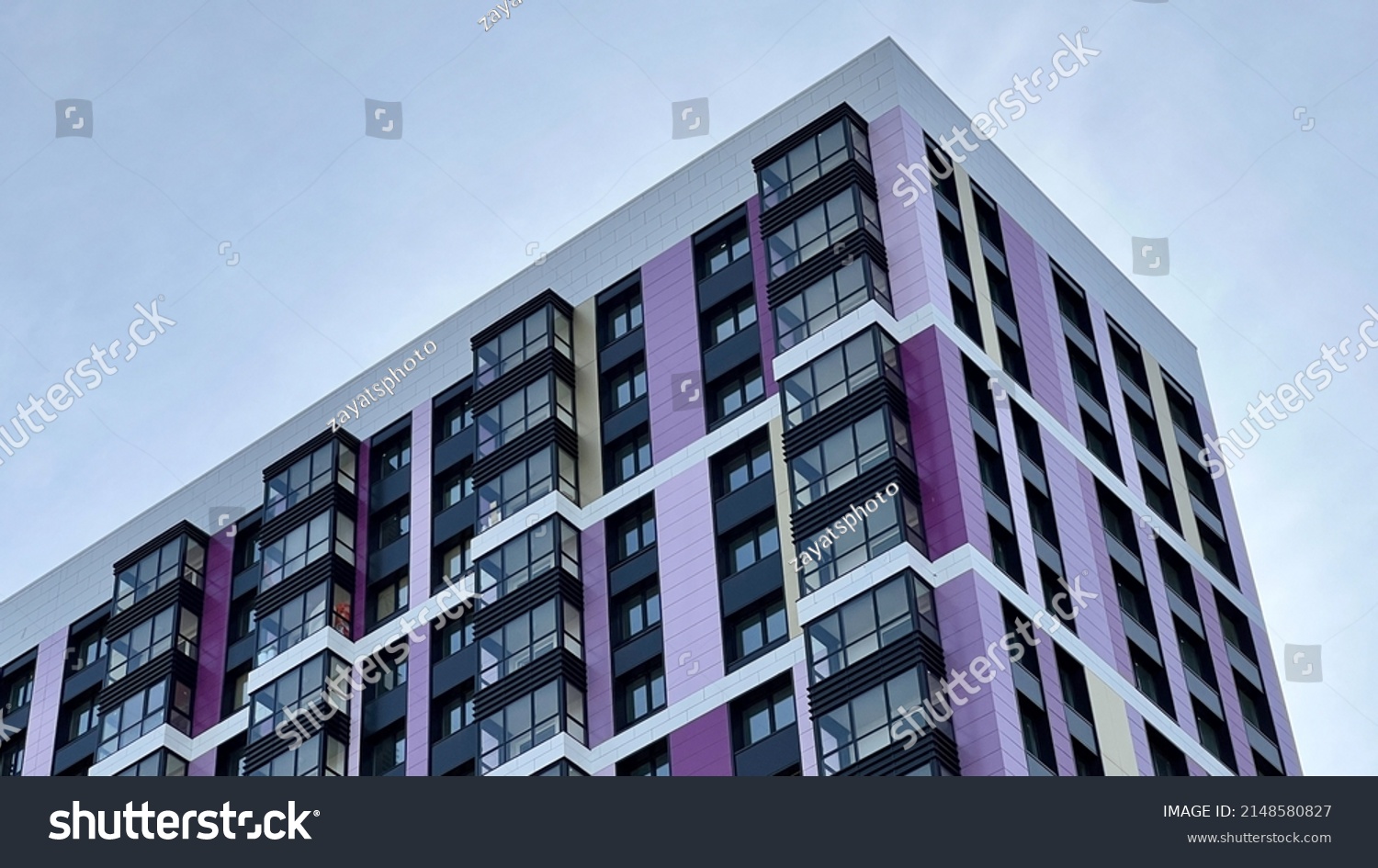 The facade of the building in purple,geometric patterns from windows and balconies, the colored wall of a modern multi-storey residential building, the abstract texture of the facade of the house #2148580827