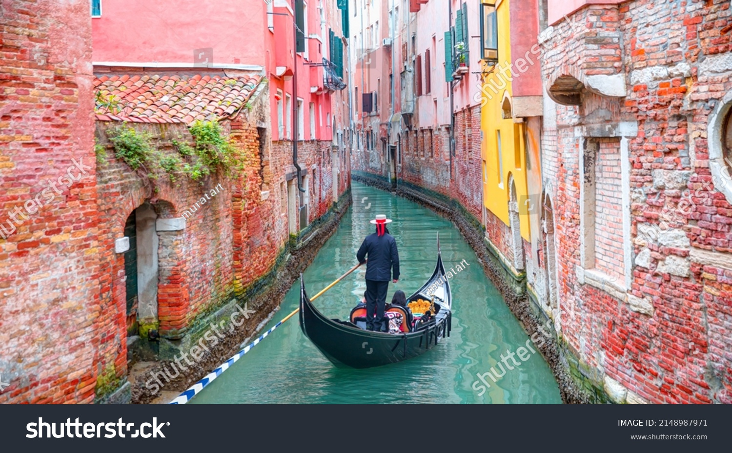 Venetian gondolier punting gondola through green canal waters of Venice Italy #2148987971