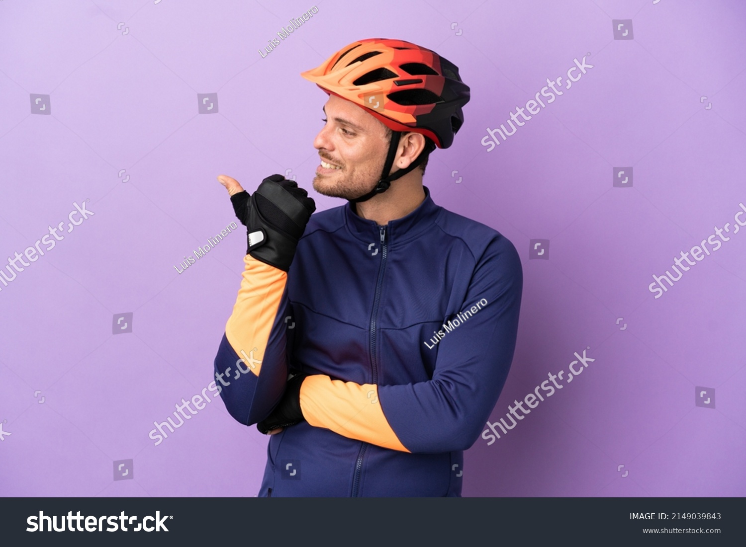 Young Brazilian cyclist man isolated on purple background pointing to the side to present a product #2149039843