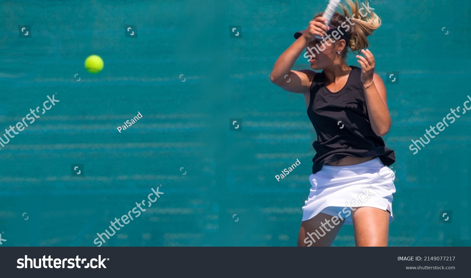 A girl plays tennis on a court with a hard blue surface on a summer sunny day
 #2149077217