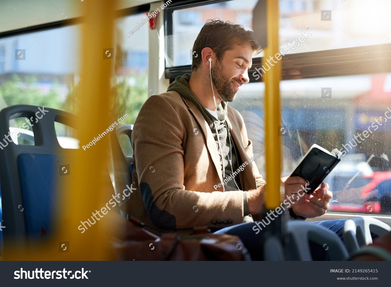 Checking out the best tourist spots. Cropped shot of a handsome young man reading a book during his morning bus commute. #2149265415