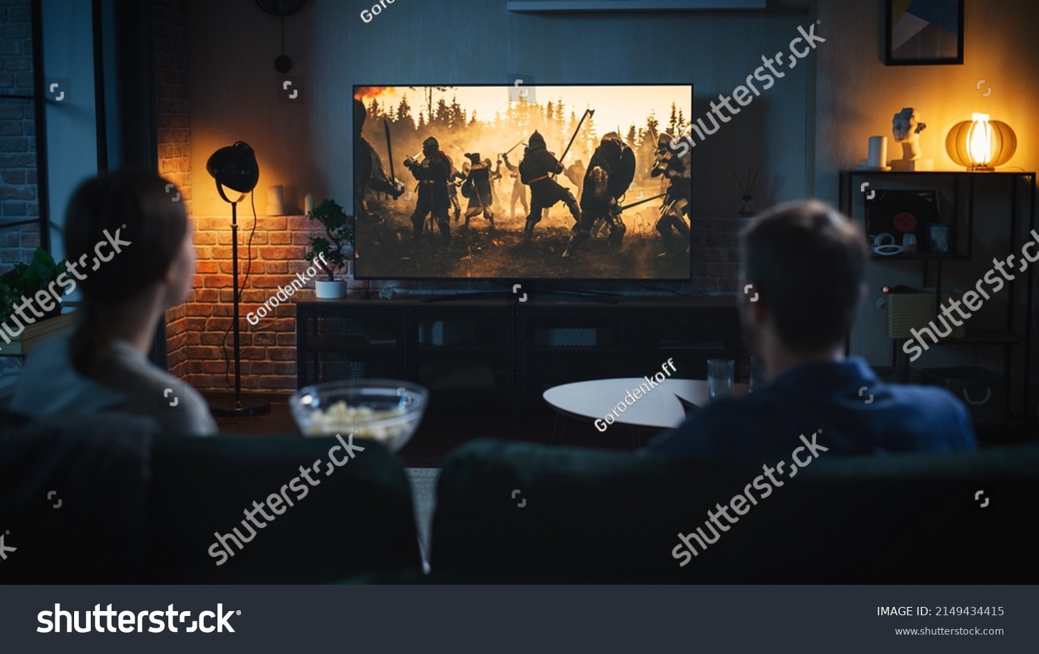 Authentic Couple Spending Time at Home, Sitting on a Couch and Watching Latest Blockbuster on Flat Screen Television Set. Man and Woman Streaming Movie or Show Using Home Cinema System. #2149434415