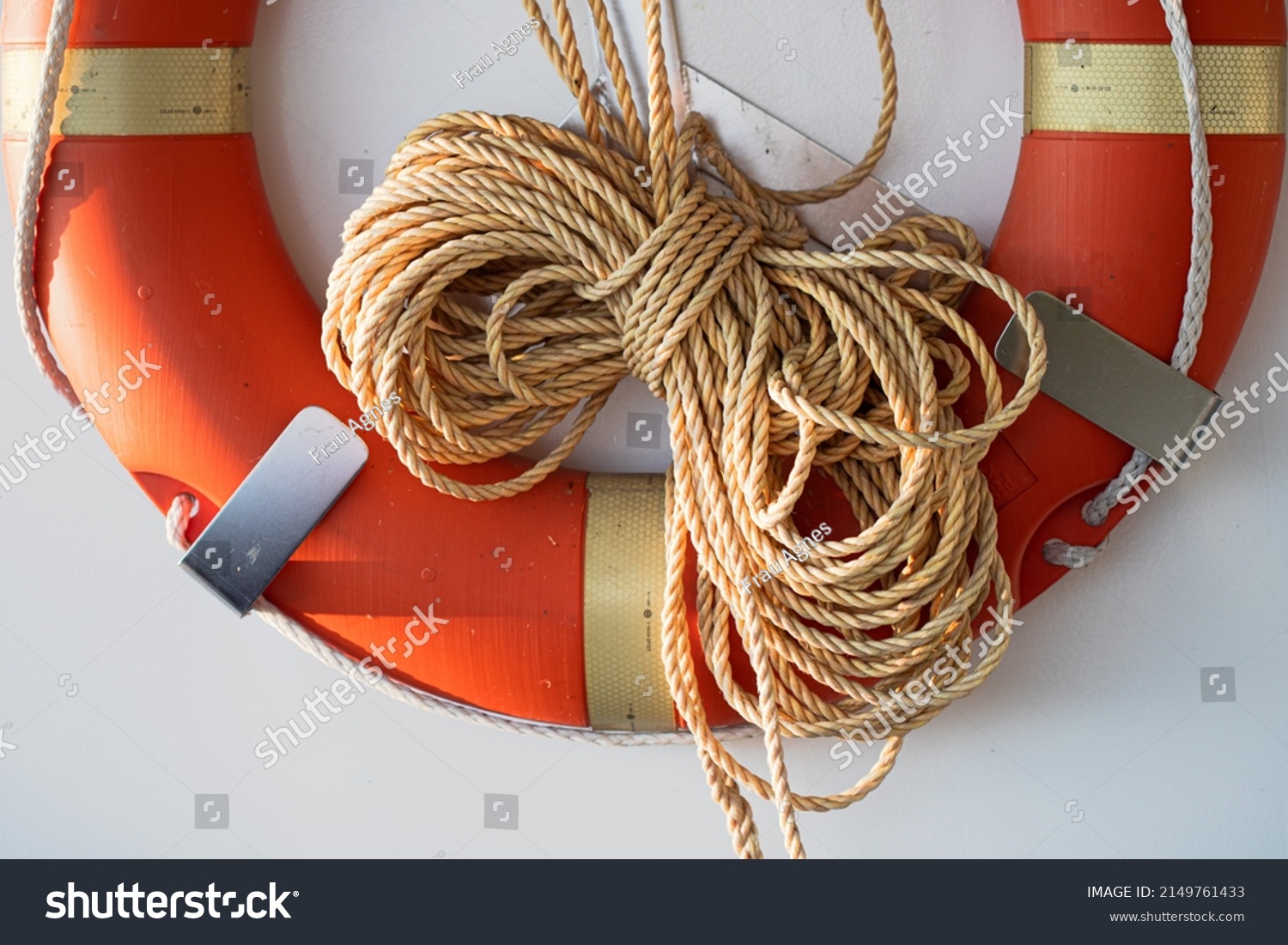 Coiled rope on a boat. Yellow rope and an orange lifebuoy on white wall of a sailboat of marina. Classic yacht or nautical vessel lifeguard resque equipment.  #2149761433