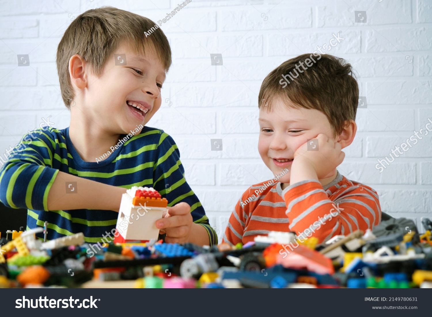Two boys sit down at the table and assemble the designer. Children laugh, are joyful, they have fun doing things together, playing and building from details. #2149780631