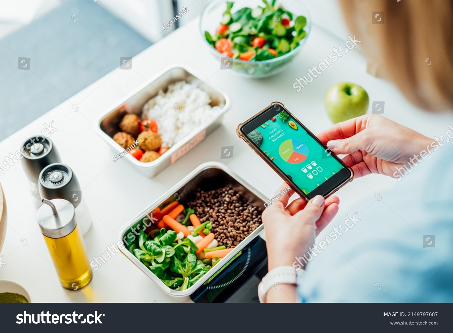 Healthy diet plan for weight loss, daily ready meal menu. Woman using meal tracker app on phone while weighing lunch box cooked in advance on kitchen scale. Balanced portion with dish. Pre-cooking #2149797687