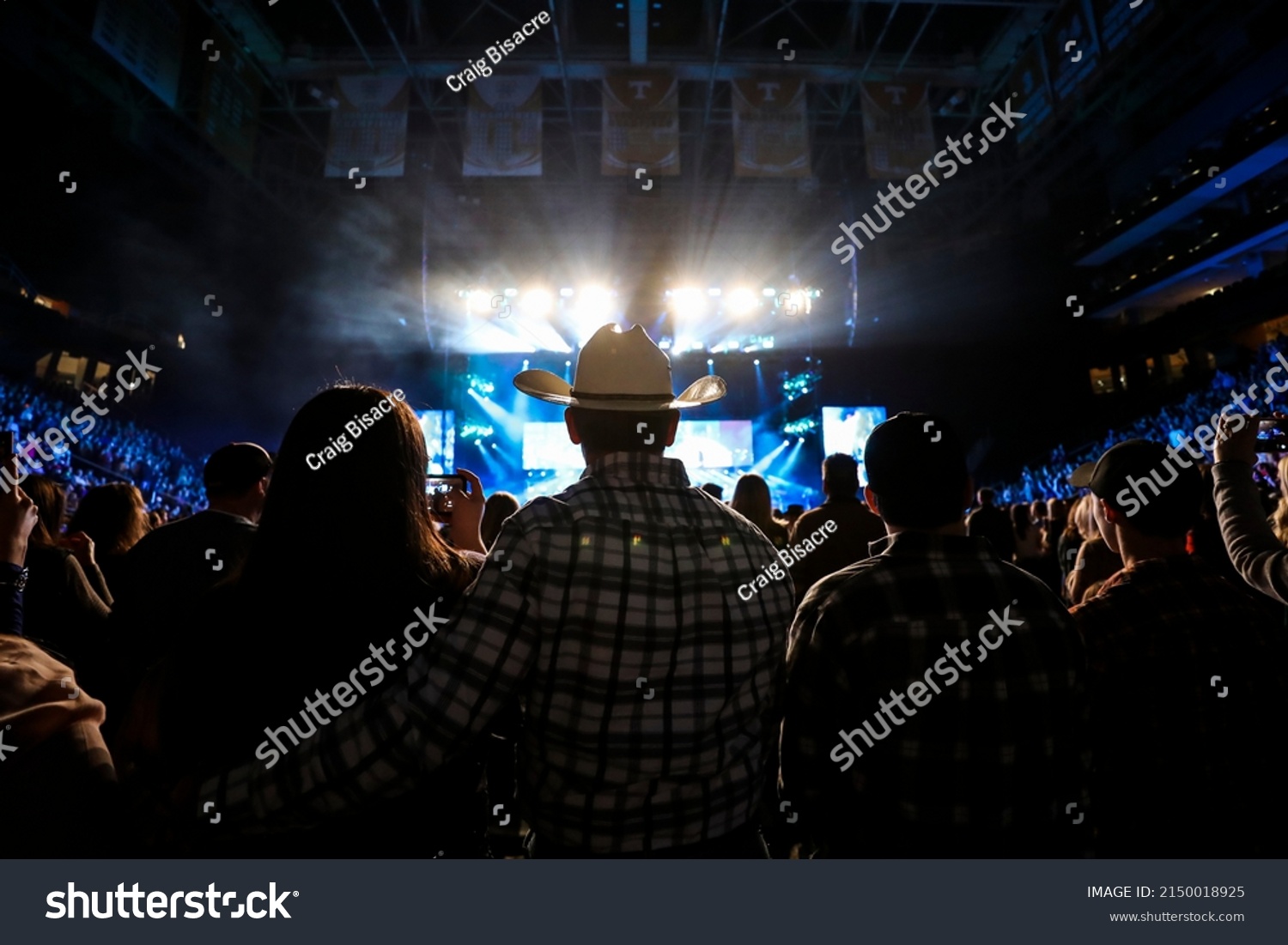 A country music fan watches a live concert wearing a cowboy hat. #2150018925