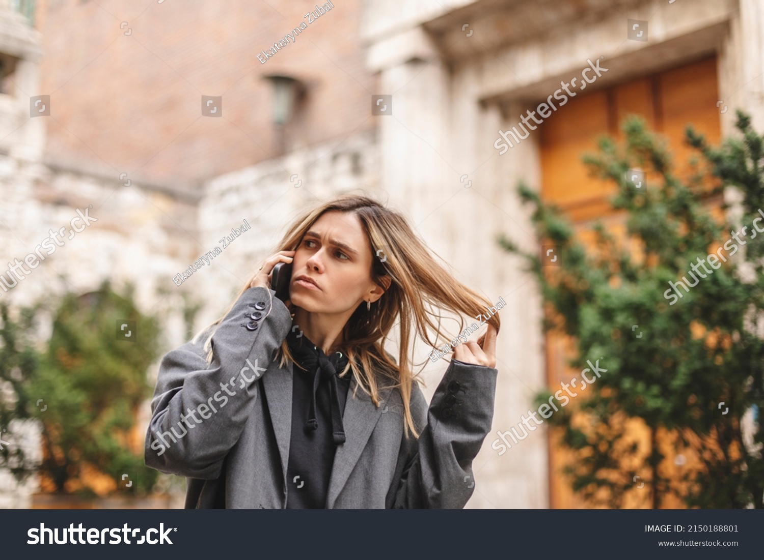 Upset woman. Woman talking sad by the bad news she hear on the cell mobile phone. Gloomy girl short hair wear grey suit and twisting a lock of hair on her finger. #2150188801