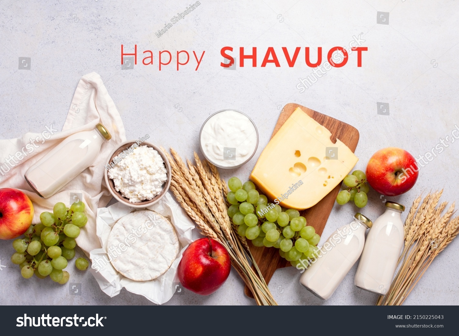 Shavuot flat lay with dairy products, first fruits and wheat on light gray background. Jewish Shavuot holiday frame with dairy foods and fruits and quote happy Shavuot, top view #2150225043