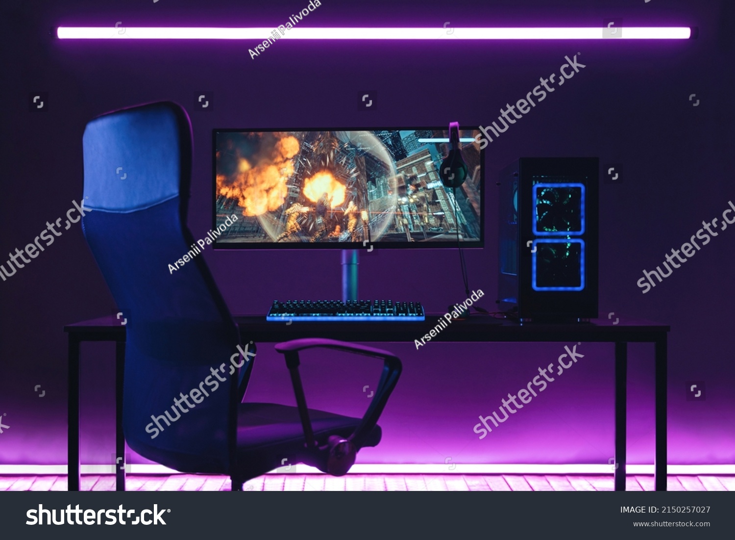 General view of home workplace of pro gamer with professional gaming setup on desktop. Modern powerful PC full RGB light inside, display with shooter game, armchair. Gaming studio of cyber sportsman #2150257027
