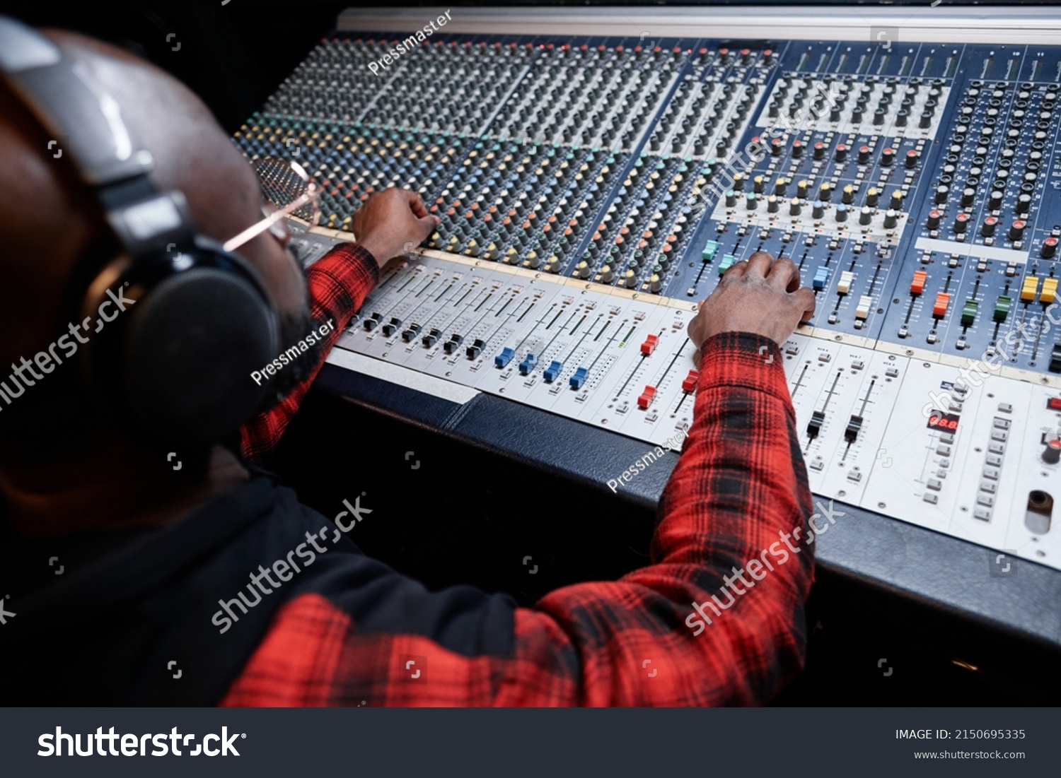 Professional sound engineer producing recording in studio adjusting sound settings at mixing console #2150695335