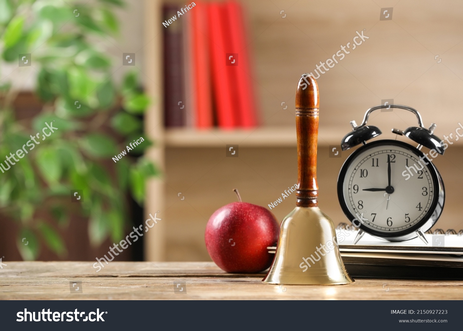Golden school bell, apple, alarm clock and notebooks on wooden table in classroom, space for text #2150927223