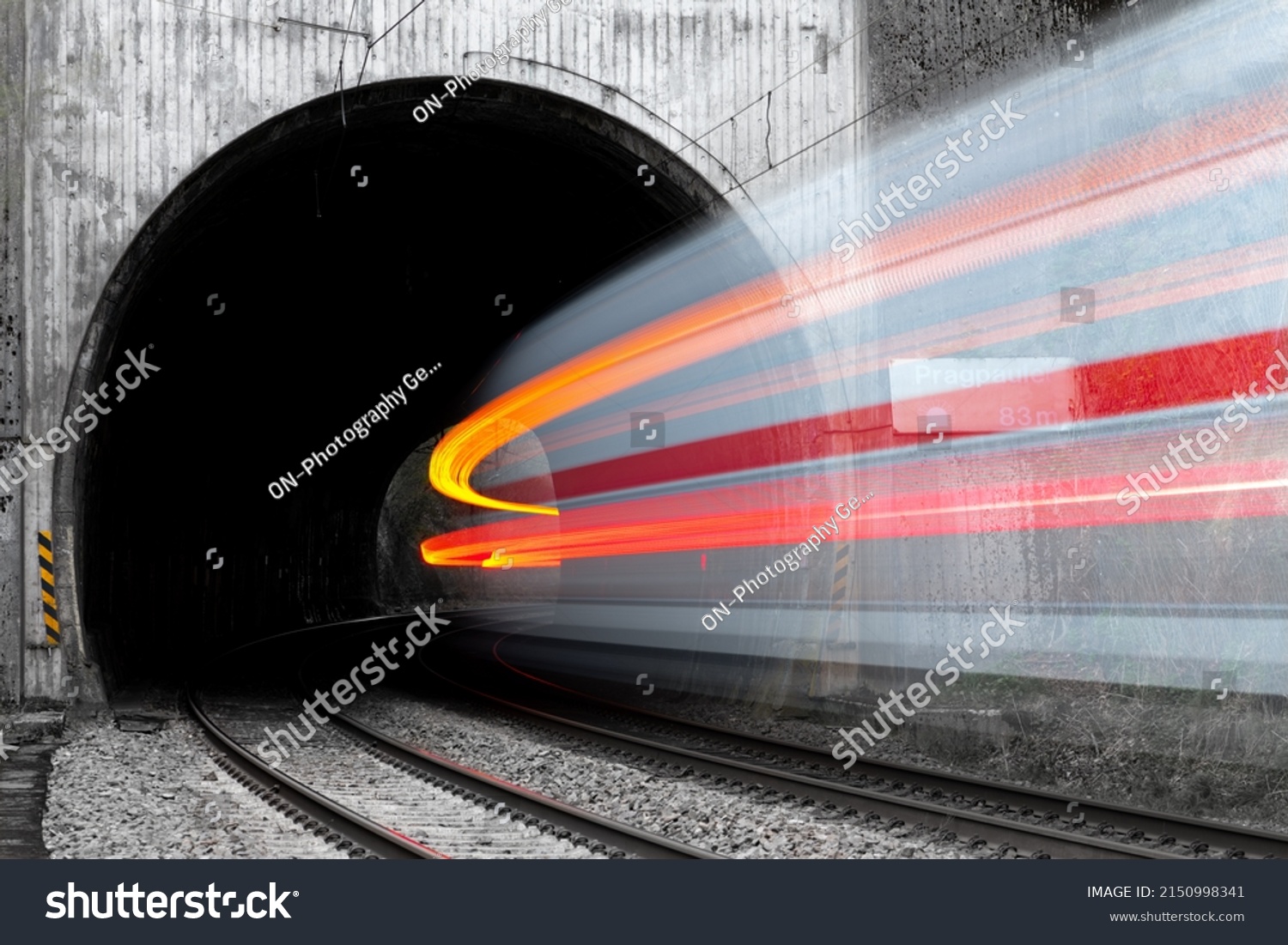 Fast train entering a tunnel with old concrete portal near Altena Germany in rural Lenne valley. Long time exposure shows motion of white and red passenger train in a curve vanishing in the darkness. #2150998341