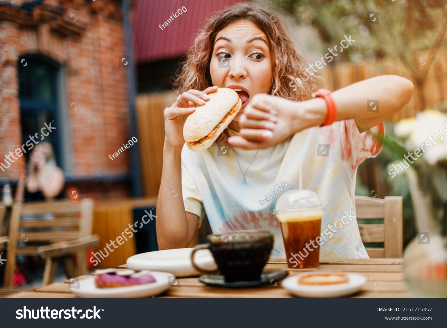 A girl in a hurry bites a burger on the run in a fast food cafe and looks at the smart watch. Late for a meeting and punctuality and digestive problems #2151715357