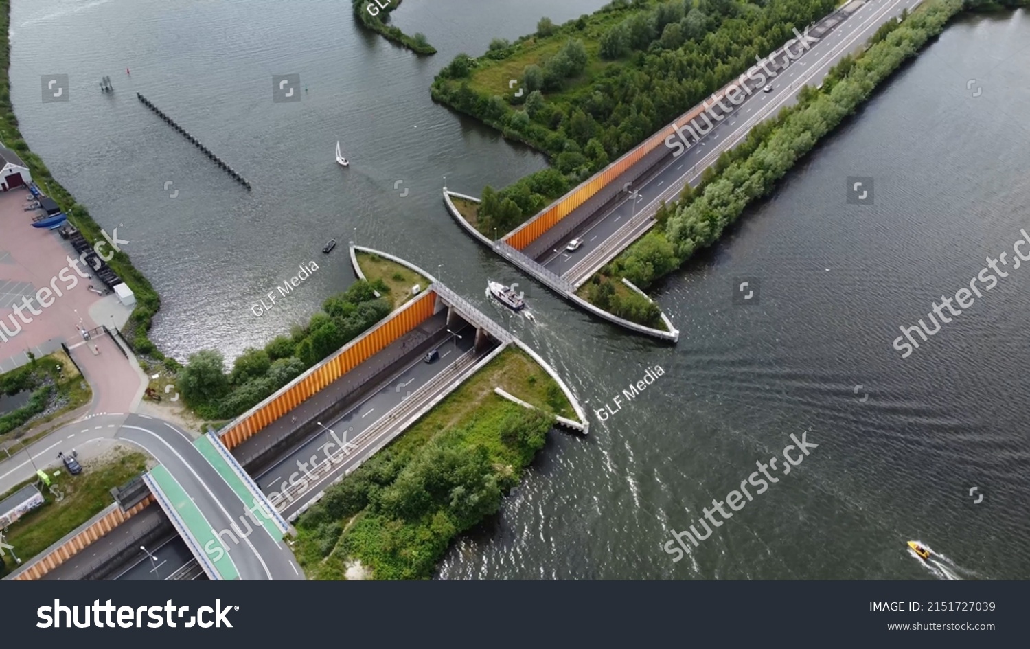 Aerial drone view of modern aqueduct or water bridge is constructed to convey watercourses across gaps showing a sailboat moving over the infrastructure and vehicles cars driving under 4k quality #2151727039