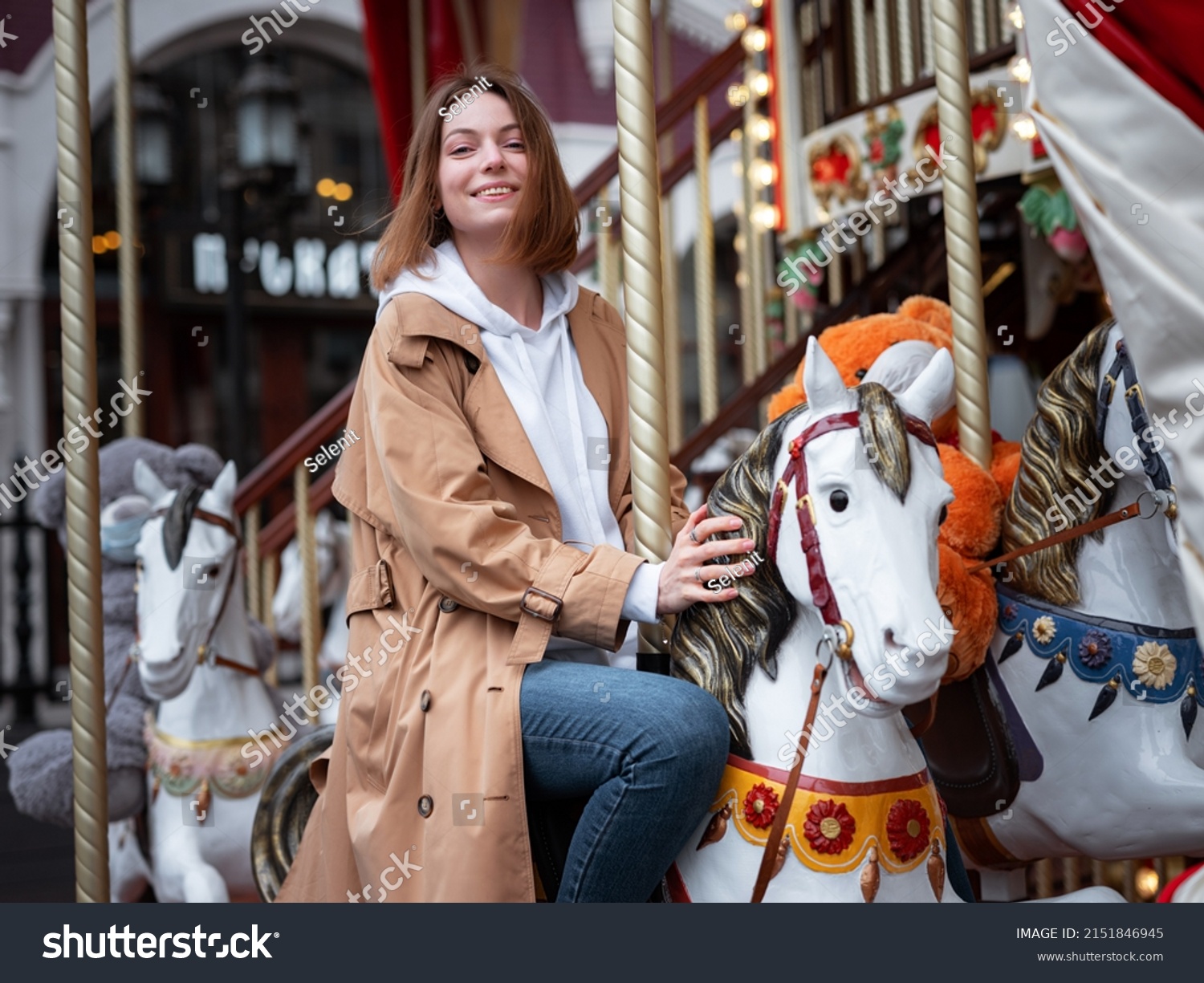 Beautiful woman in beautiful beige coat walk in autumn cloudy Moscow, enjoys and has fun on carousel. Street style. Travel to Russia concept. #2151846945