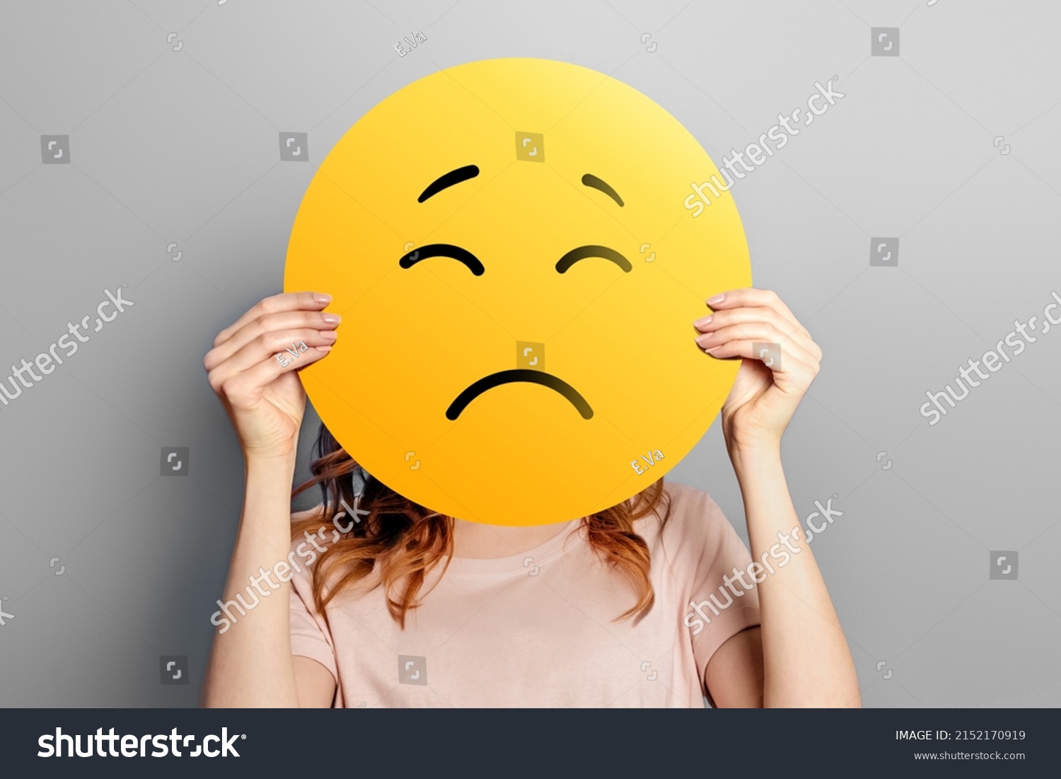 Sad emoji. Girl holds a yellow emoticon with sad face isolated on a gray background. unhappy emoji #2152170919