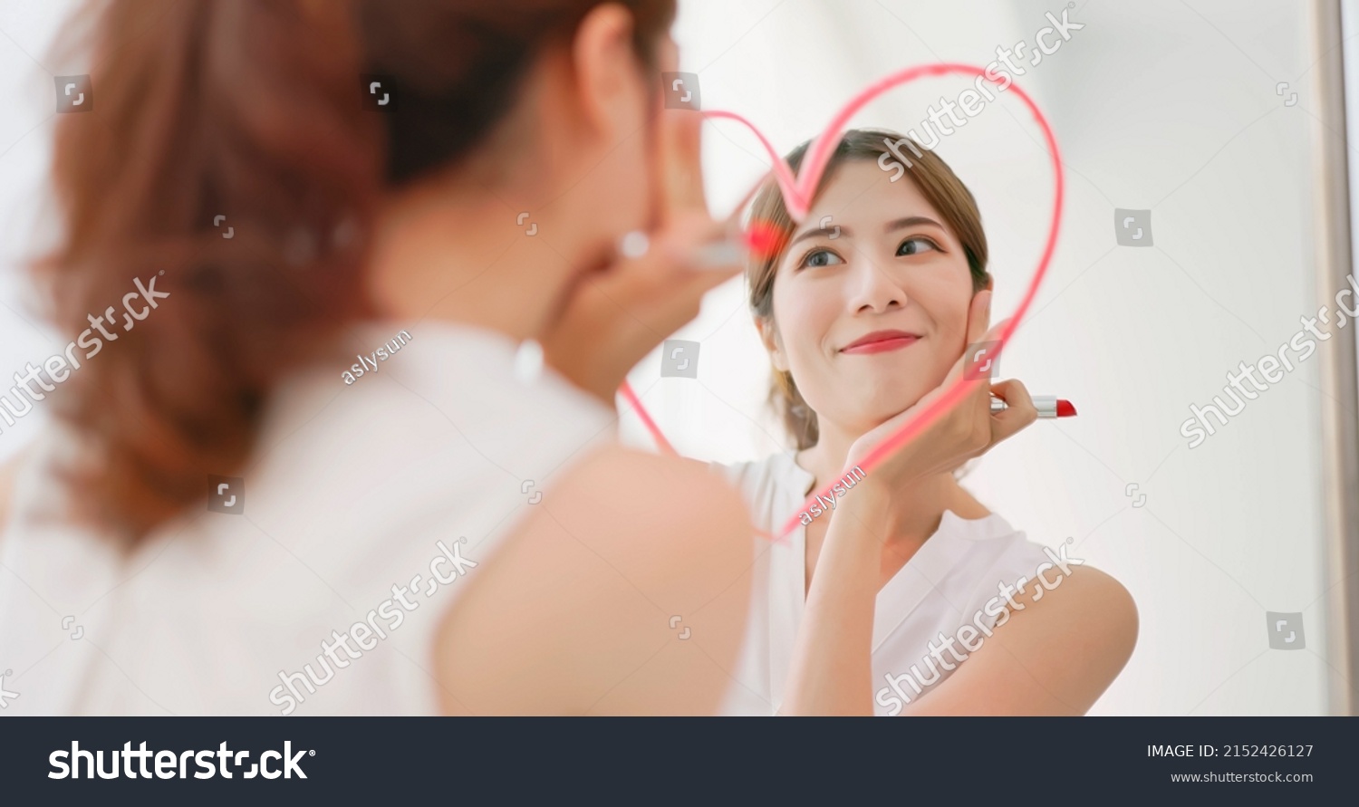 asian woman with brunette ponytail draws a heart shape use lipstick on the mirror and look at herself feeling confident self love #2152426127