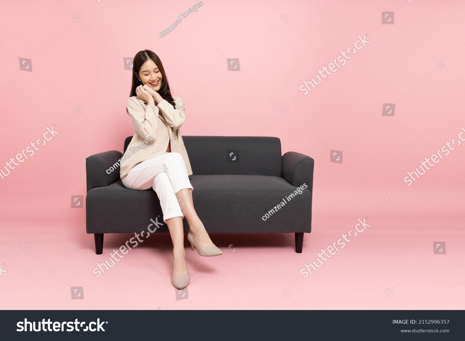 Excited Asian businesswoman sitting on sofa isolated on pink background #2152996357