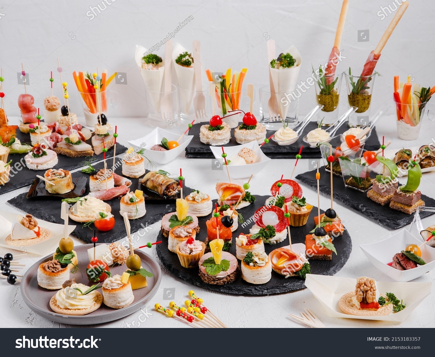 Mini snacks on a white background. Cold appetizer. On a black serving board. Snacks for public catering . Catering. Buffet table. Catering. #2153183357