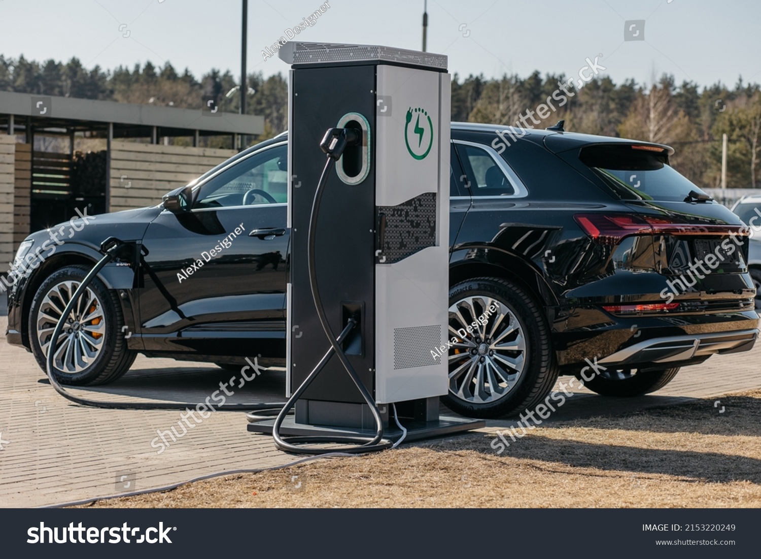 A photograph of an electric car being charged from a portable electric vehicle charging station located right in a parking lot in the city. #2153220249