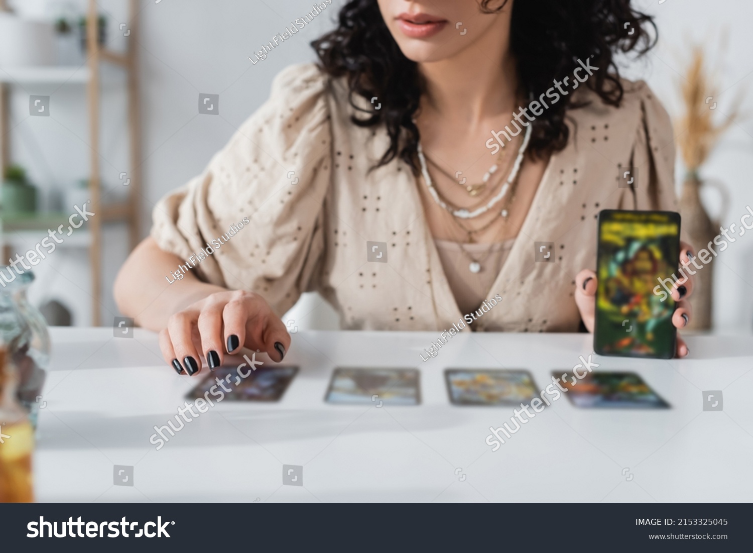 Cropped view of soothsayer holding blurred tarot cards near table #2153325045