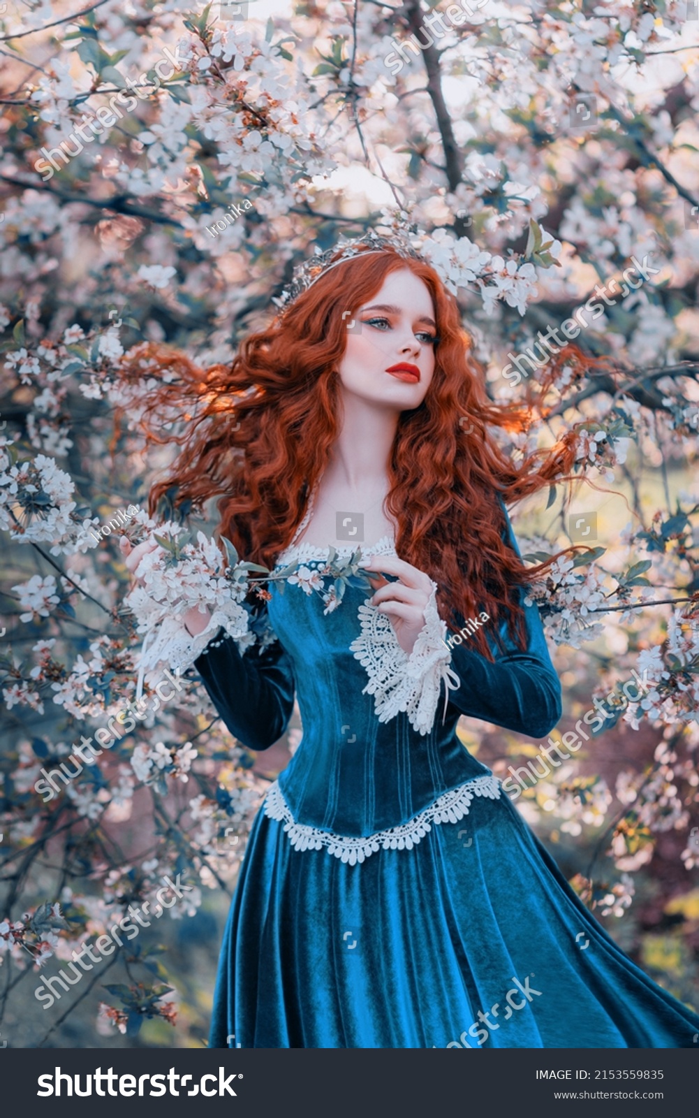 Fantasy portrait red-haired girl romantic princess stands in spring flowering garden. Blooming green tree flowers. Long hair red lips pale skin face woman queen medieval vintage creative design dress #2153559835