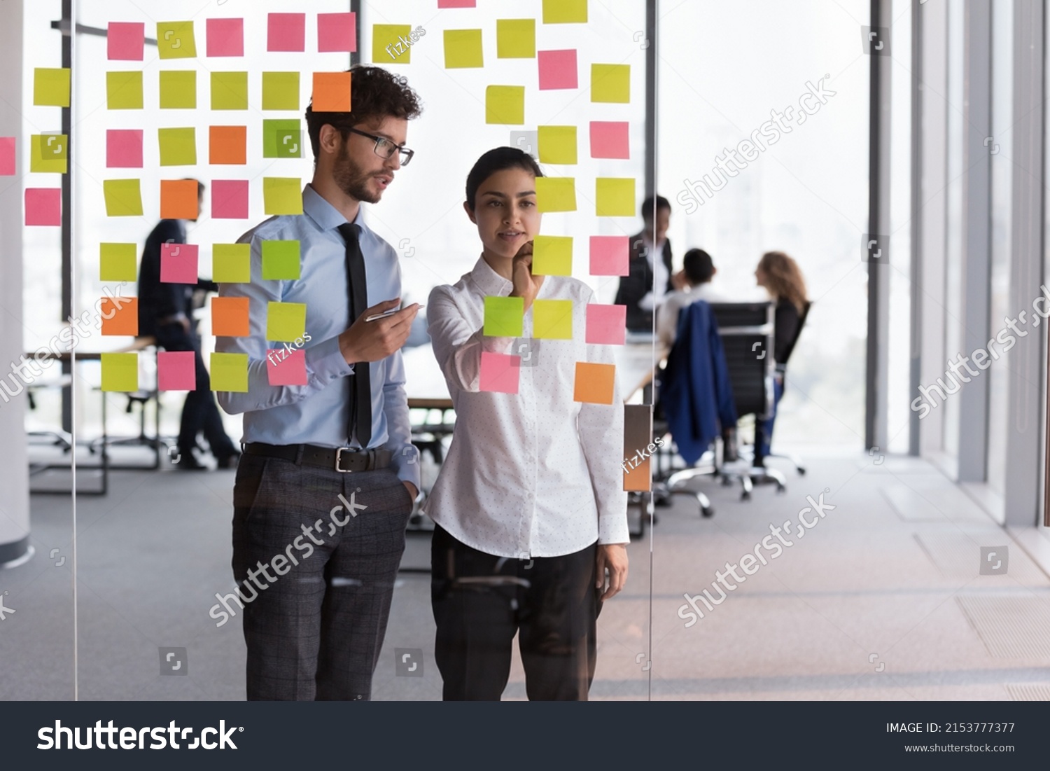 Confident Indian mentor woman teaching young Intern guy, training to use Kanban board for planning tasks, project strategy. Diverse millennial employees using scrum management for teamwork #2153777377