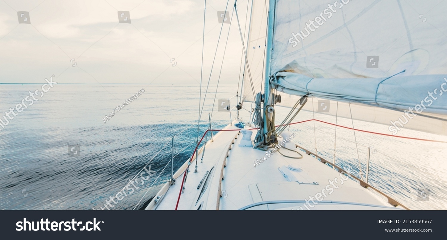 White sloop rigged yacht sailing at sunset. Clear sky after the storm. View from the deck to the bow, mast, sails. Transportation, travel, cruise, sport, recreation, leisure activity, racing, regatta #2153859567