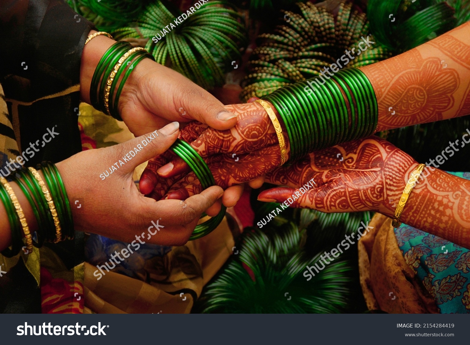 At a pre wedding ceremony a lady bangle seller is putting green glass bangles on the henna decorated hands of  a maharashtrian bride. They 
symbolize fertility and prosperity in Indian culture.       #2154284419