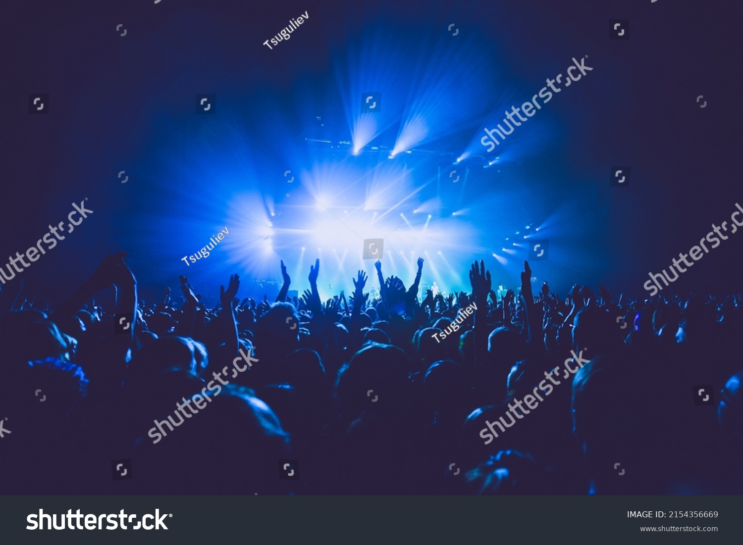 A crowded concert hall with scene stage lights in blue tones, rock show performance, with people silhouette, on a dance floor air during a concert festival #2154356669