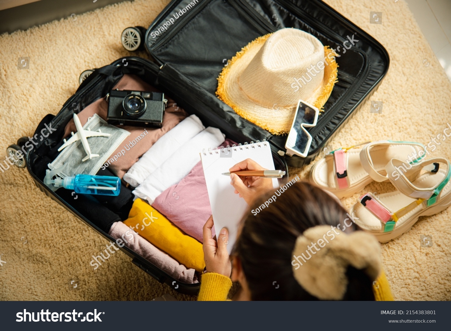 Making check list of things to pack for travel. Woman writing paper take note and packing suitcase to vacation writing paper list sitting on room, prepare clothes into luggage, Travel vacation travel #2154383801