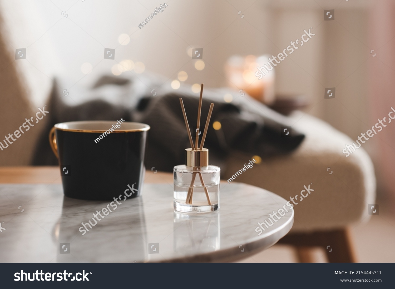 Bamboo sticks in bottle with scented candles and cup of tea on marble table closeup. Home aroma. Aromatherapy. Apartment living.  #2154445311