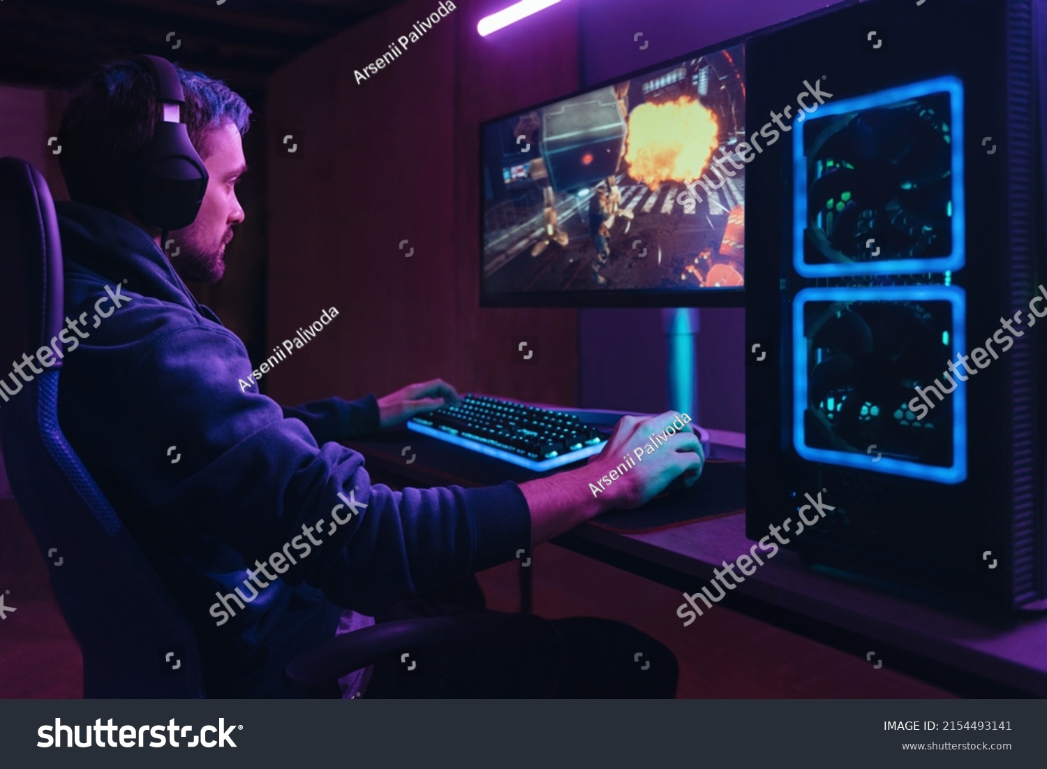 Young concentrated cyber sportsman playing in FPS video game on his personal computer in dark neon room. Pro gamer participating in online esport competition. Cyber games championship event concept #2154493141