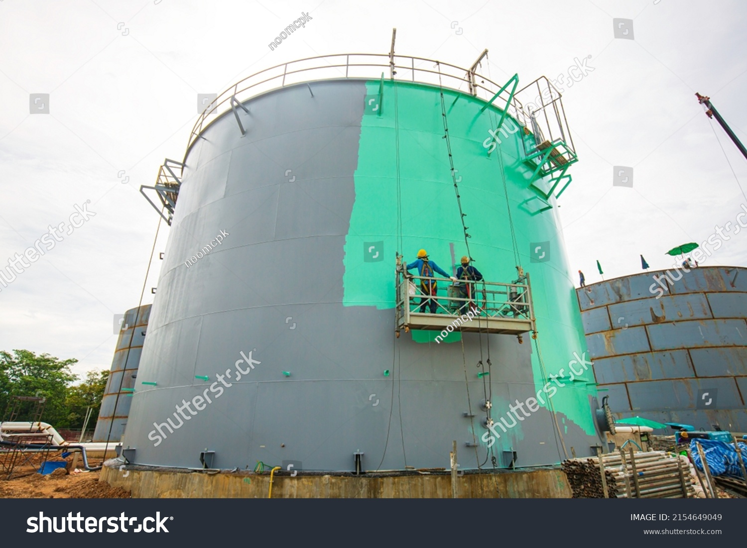 The male worker takes the cable car holding an industrial painting brush used for shell plate tank oil surface surface green color coating. #2154649049