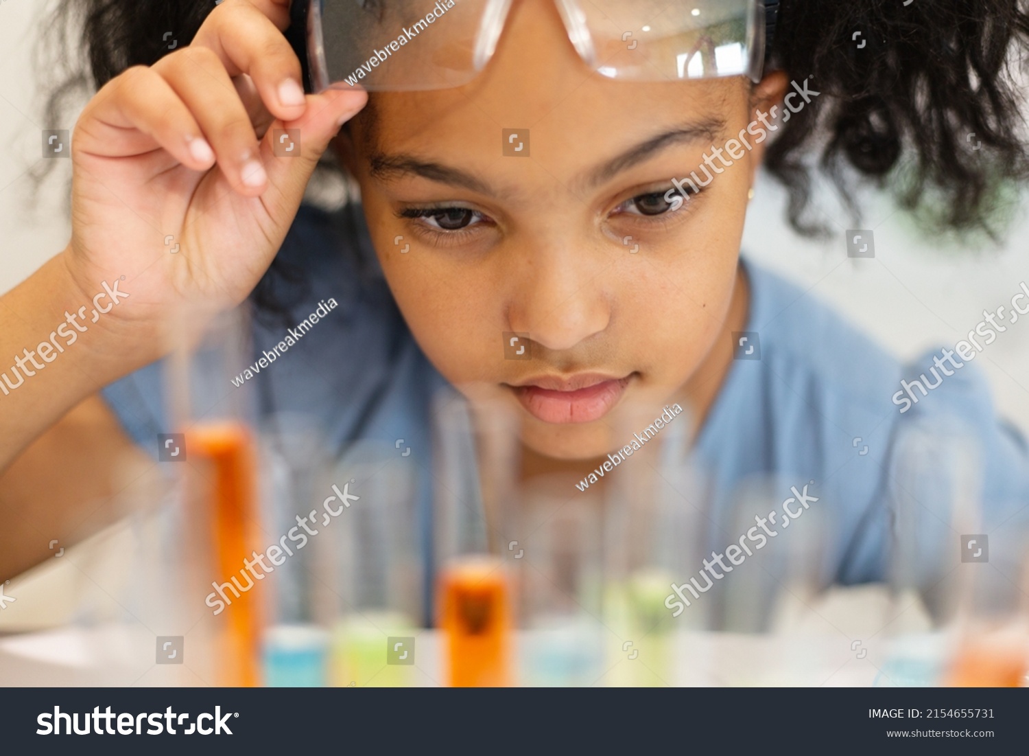 Close-up of biracial elementary schoolgirl looking at chemicals in test tubes during chemistry class. unaltered, education, learning, scientific experiment, stem, protection and school concept. #2154655731