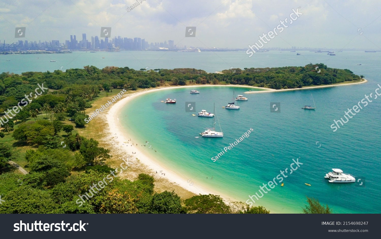 Aerial picture of Lazarus Island in Singapore. View to the beach. Sunny warm day. Turquoise water and green forest. Boats anchored in shore water. The center of Singapore is visible on the horizon. #2154698247