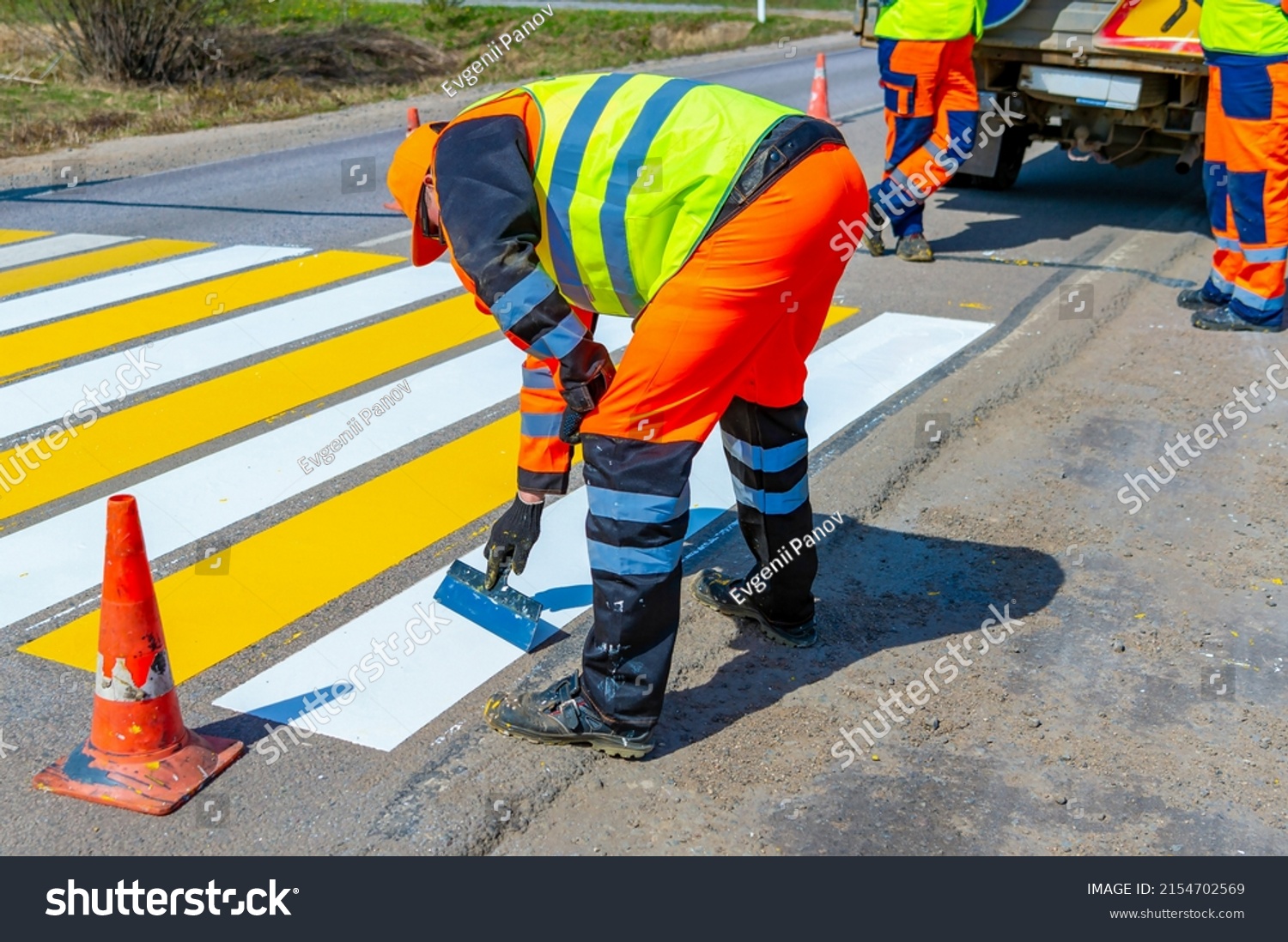 A road worker paints, repairs a pedestrian crossing on an asphalt surface on a city street. #2154702569
