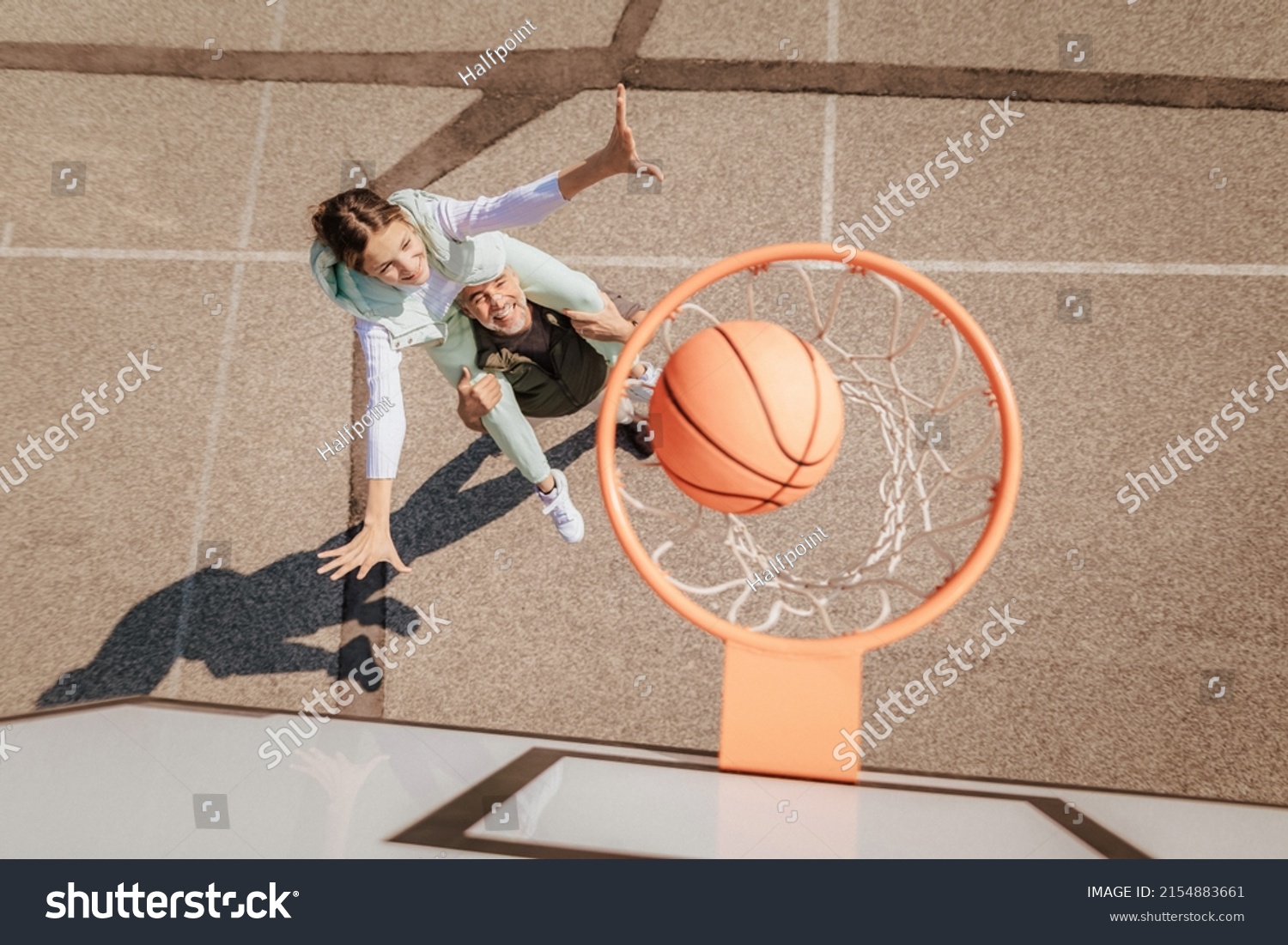 Father and teenage daughter playing basketball outside at court, high angle view above hoop net. #2154883661