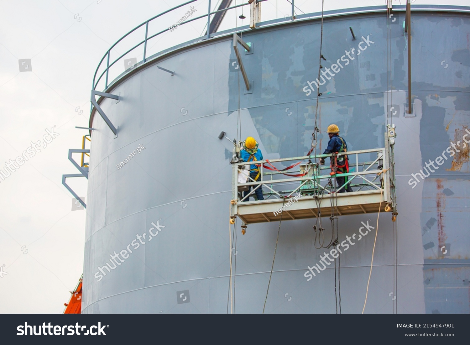 The male worker takes the cable car holding an industrial painting brush used for shell plate tank oil surface painted gray color coating. #2154947901