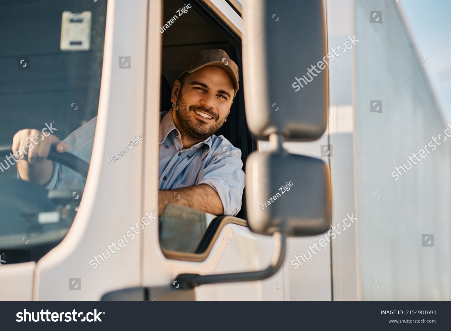 Happy professional truck driver driving his truck and looking at camera. Copy space. #2154981693