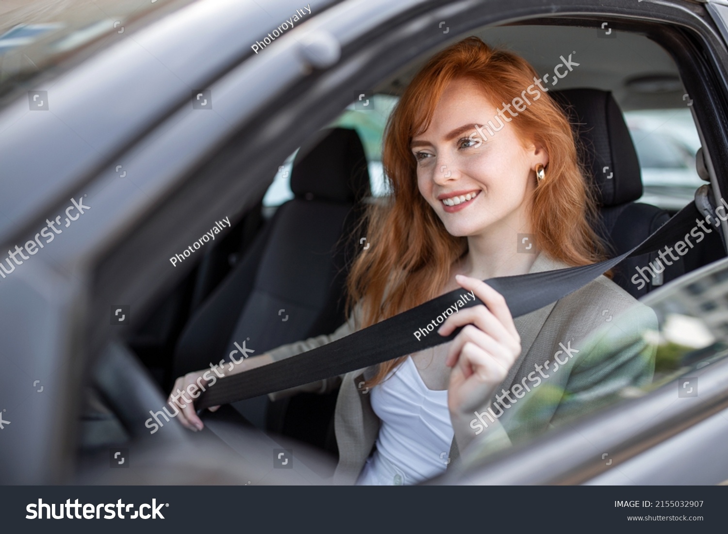 Young woman sitting on car seat and fastening seat belt, safety concept. Woman fastens a seat belt in the car. Caucasian woman driver fastening car seat belt while sitting behind the wheel car. #2155032907