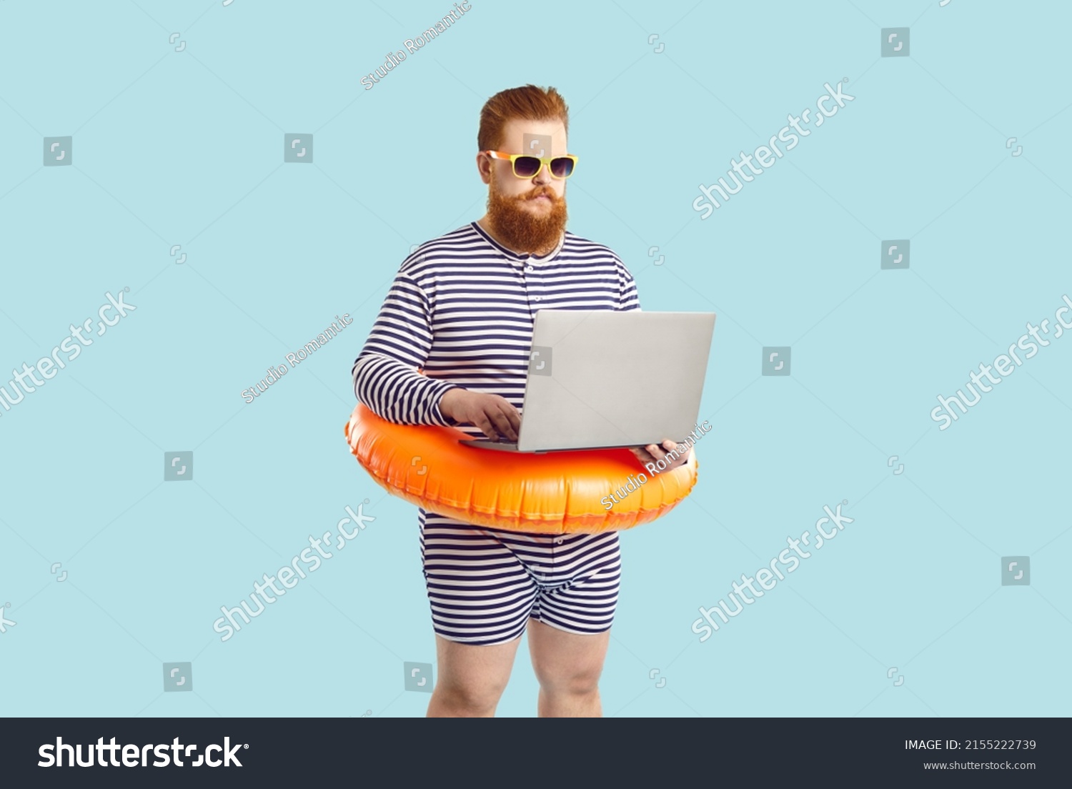 Funny man finds time for business during summer holiday at seaside. Serious chubby entrepreneur working on computer while on vacation. Busy plus size guy in striped swimsuit using his laptop at beach #2155222739