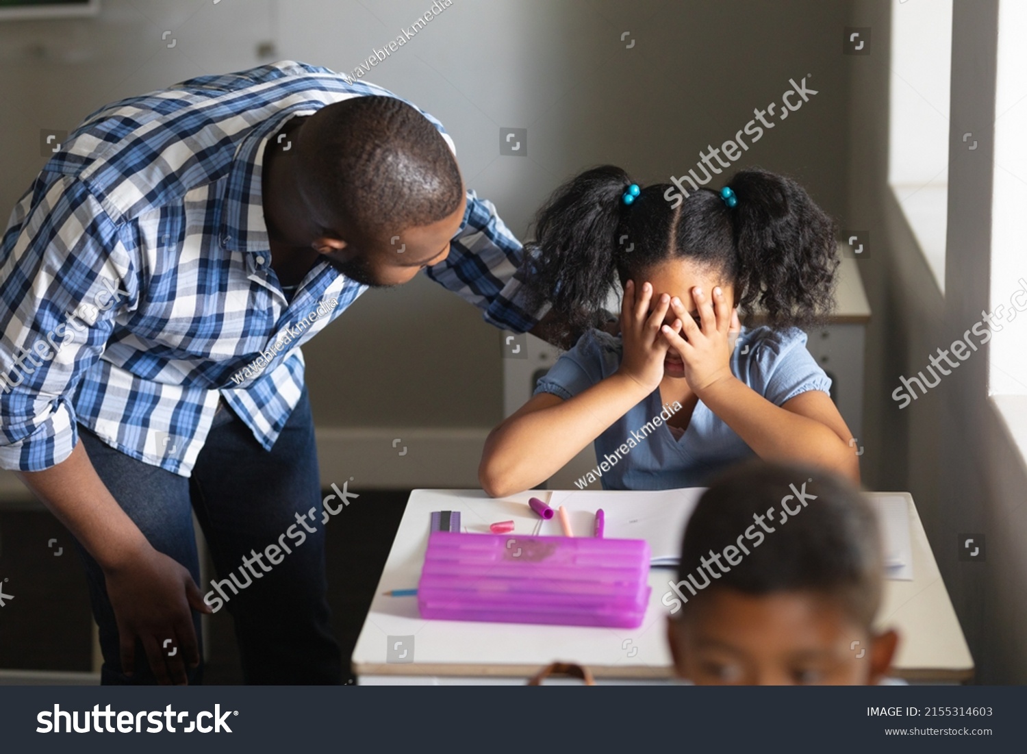 African american young male teacher consoling sad biracial elementary schoolgirl sitting at desk. unaltered, education, communication, childhood, sadness, depression, failure and school concept. #2155314603
