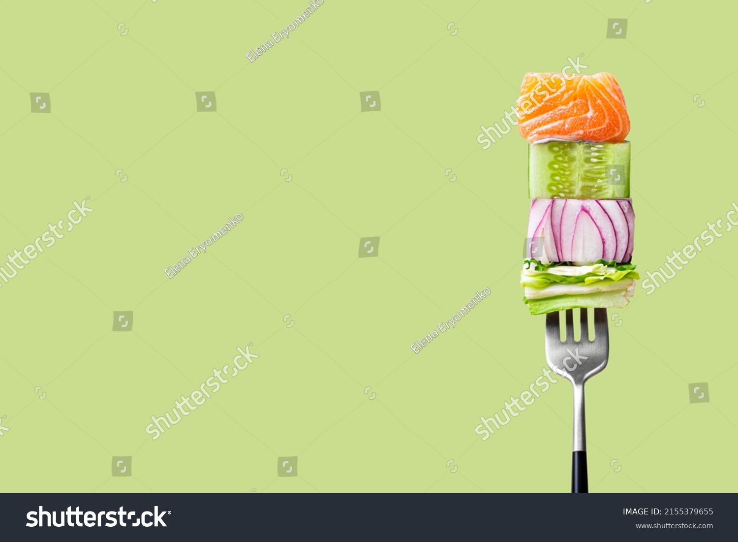 Close-up of fork with food on it: delicious fillet salmon, cucumber, onion, green salad on green background. Concept of healthy diet and clean eating, balanced nutrition space for text #2155379655