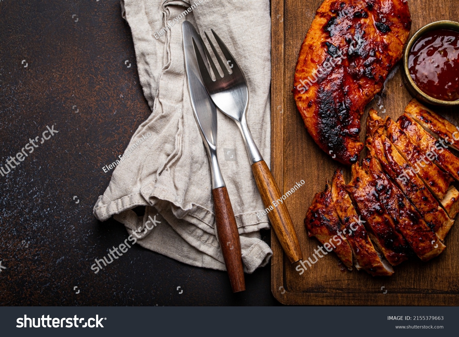 Grilled turkey or chicken marinated fillet with red sauce served and sliced on wooden cutting board on stone brown background from above, poultry breast barbecue space for text #2155379663