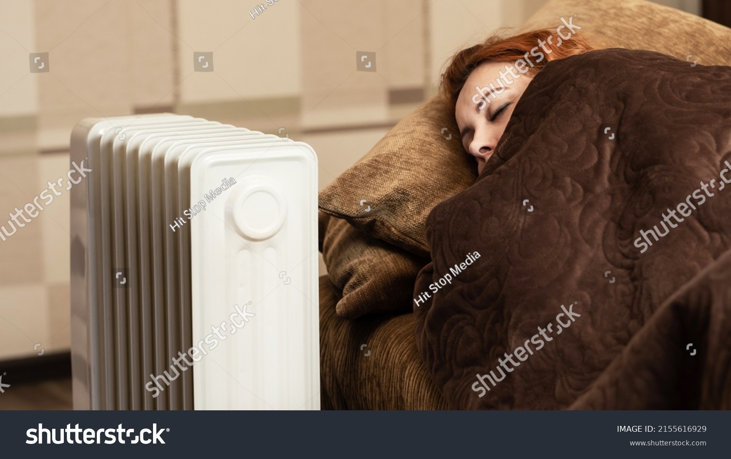 A young girl sleeps wrapped in a blanket near the heating radiator at home. Heating season. #2155616929