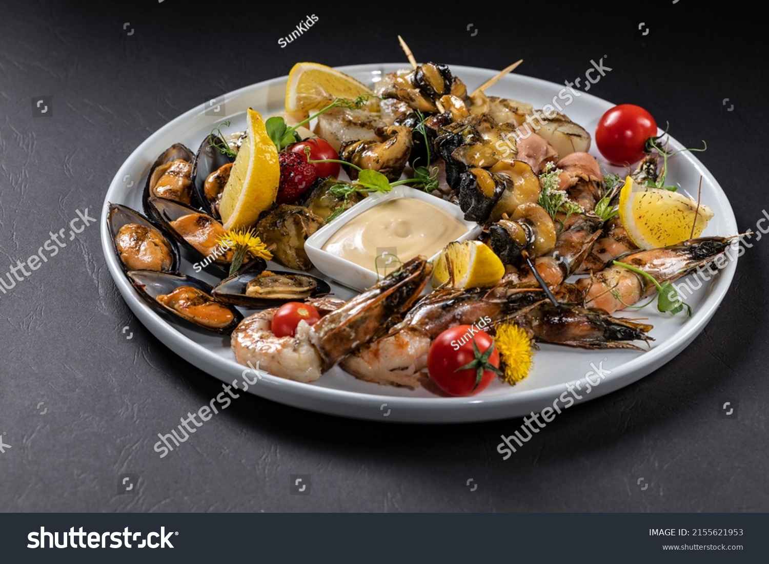 Set of seafood from mussels, shrimps, scallops and rapans with lemon and tomatoes on a white plate. Black background #2155621953