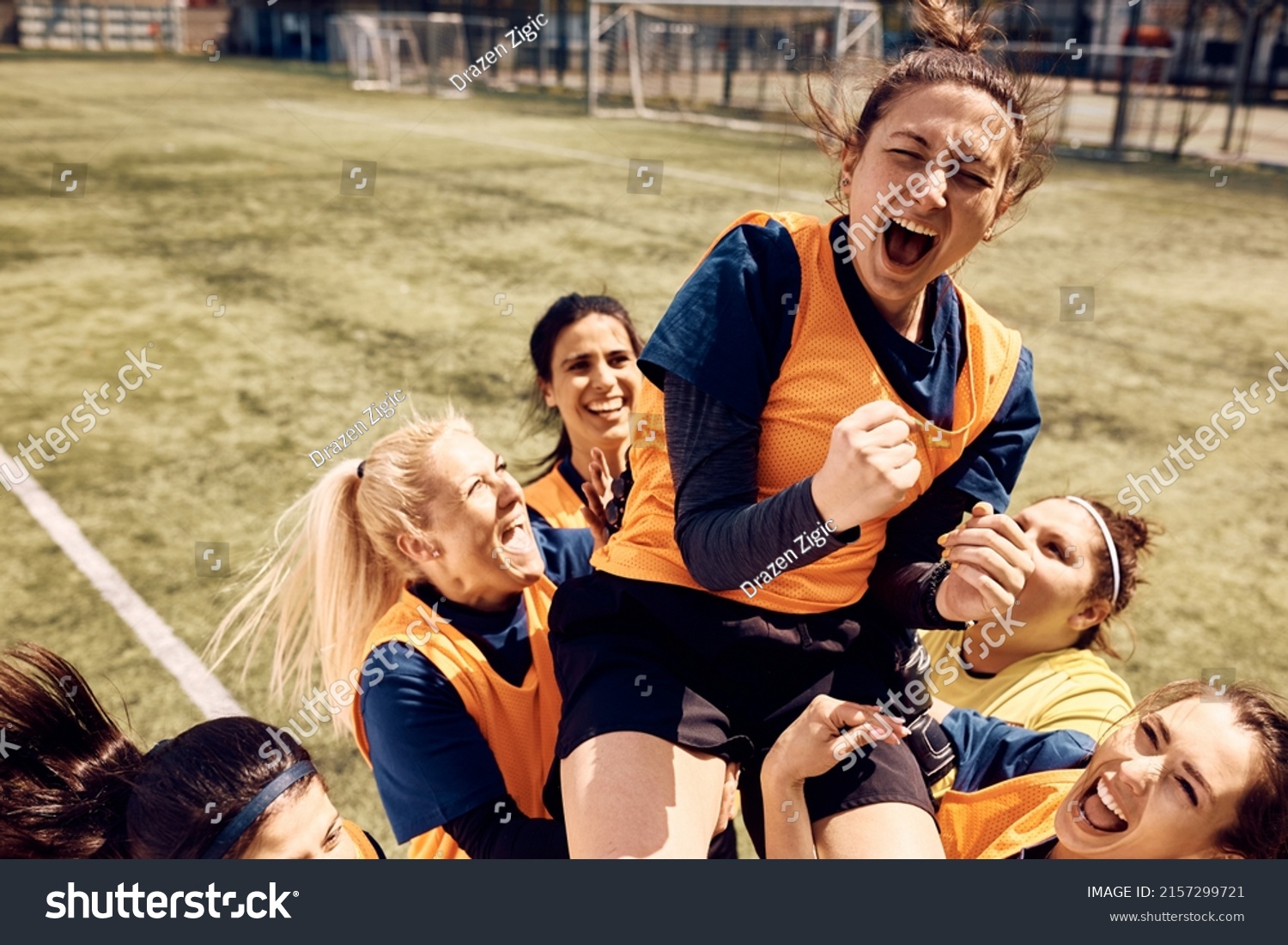 Cheerful team of female soccer players celebrating victory and carrying on of teammates who is shouting out of joy on stadium. #2157299721